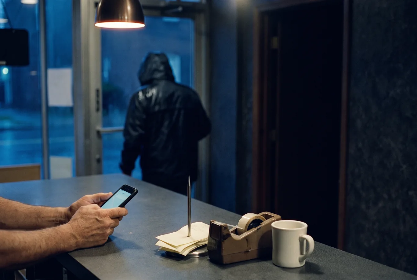Hands hold a phone at a shop counter at night while a customer walks out through the glass door
