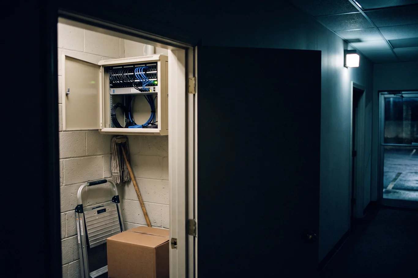 A small practice server cabinet in a back room, one status light on, the door standing open
